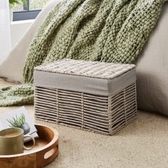 a wicker storage box on the floor next to a bed with a green blanket