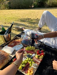 two people sitting at a picnic table with food and wine