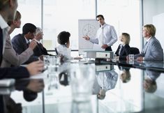 a group of people sitting around a conference table with a whiteboard in the middle