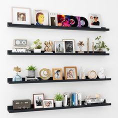 three black shelves with pictures, books and other items on them against a white wall