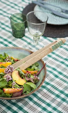 a salad with peaches and spinach in a bowl on a checkered table cloth