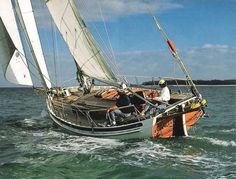 an orange sailboat in the middle of the ocean with people on it's deck