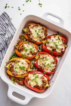 stuffed bell peppers in a white casserole dish with cheese and herbs on top