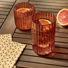 three glasses filled with blood oranges sitting on top of a wooden table next to two slices of grapefruit