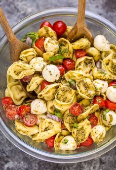 a glass bowl filled with pasta salad and topped with cherry tomatoes, mozzarella cheese and basil