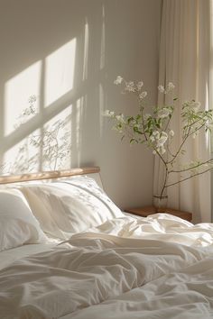 a bed with white sheets and pillows next to a vase with flowers on top of it