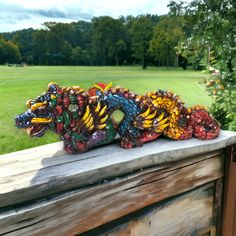 three colorful dragon figurines sitting on top of a wooden fence in front of a green field