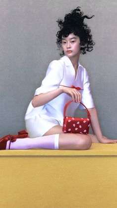 a woman sitting on top of a yellow table holding a red purse and posing for the camera