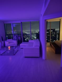 a living room filled with white furniture and purple lighting on the walls next to large windows