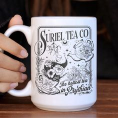 a woman is holding a coffee mug in her hand while sitting at a wooden table