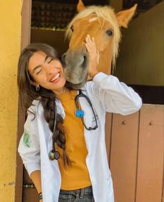 a woman in white lab coat standing next to a horse with her hand on the nose