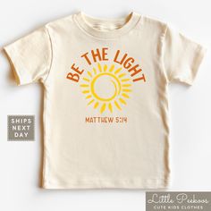 a white t - shirt with the words be the light and an orange sun on it