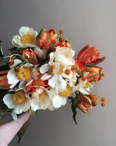 a hand holding a bouquet of white and orange flowers on a gray background with text overlay