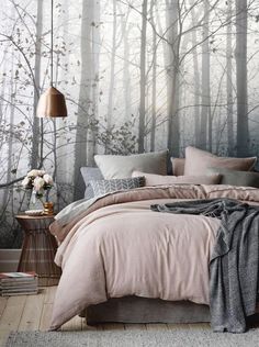 a bedroom with a bed, pillows and blankets in front of a forest wall mural