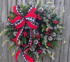 a wreath with red berries, pine cones and evergreens is hanging on a wooden fence