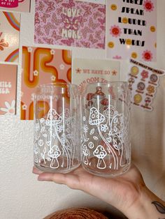 a person holding two glasses in front of a wall covered with pictures and magnets