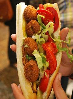 a person holding a sandwich with meatballs and vegetables on it in their hands,