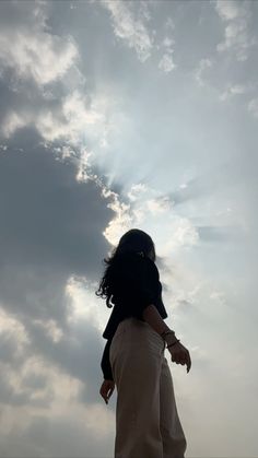 a woman flying a kite in the sky with clouds behind her and sunbeams