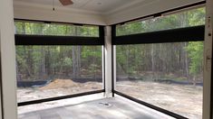 an empty room with two large windows and a dirt area in the background, looking out onto a forest