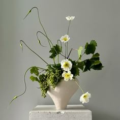 a white vase filled with lots of flowers on top of a block of concrete next to a wall