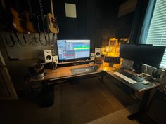 there is a computer on the desk with other equipment in front of it and guitar strings hanging from the wall