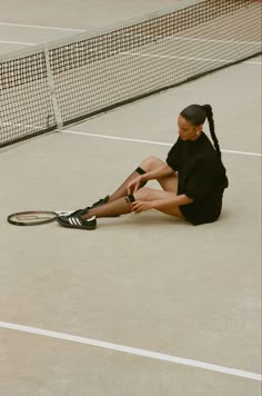 a woman sitting on the ground with a tennis racket in her hand and wearing black