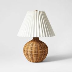 a wicker table lamp with a white shade on the top, and a light bulb at the base