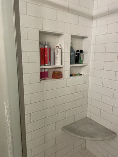 a white tiled bathroom with shelves above the shower