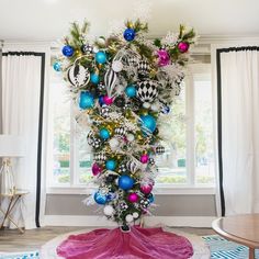 a christmas tree with ornaments in the middle of it on a rug next to a window