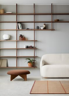 a white couch sitting in front of a wooden shelf filled with books and vases