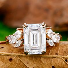 an emerald - cut diamond ring sits on top of a leaf