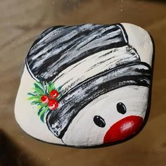 a painted rock with a clown's hat and holly berries on it, sitting on a table