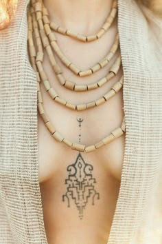 a woman with a tattoo on her chest wearing a white cardigan and wooden necklace