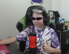 a young boy wearing headphones sitting in front of a microphone and giving the thumbs up