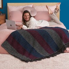 a woman laying on her bed with a laptop in front of her and an oversized blanket behind her