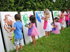 several children are painting on the side of refrigerators in front of some bushes and trees