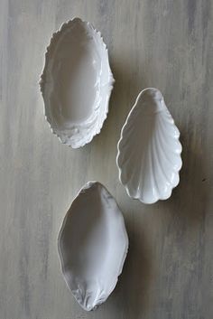 three seashells sitting on top of a wooden table next to an empty bowl