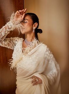 a woman in a white sari and feathered shawl poses for the camera