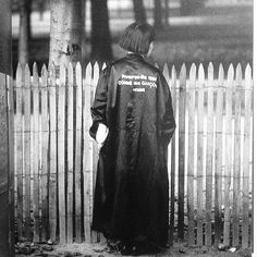 a person standing in front of a fence with a coat over their shoulders and back