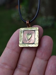 This unique "Heart in a Box" necklace is a beautifully handcrafted piece featuring a delicate brass heart surrounded by a textured brass frame, all set against a warm copper background. The brass frame is meticulously hammered to add texture and depth, making the tiny heart at its center truly stand out. The combination of copper and brass creates a stunning contrast, perfect for adding a touch of vintage charm to any outfit. This necklace is both elegant and timeless, ideal for everyday wear or as a thoughtful gift. The pendant is 3/4 inch wide, and 1 inch long (including the bale). The pendant comes with a faux-leather cord. Please choose from 16, 18 or 20 inch length. Please note the copper and brass will take on a darker patina over time but can be polished with a jewelry polishing clo Necklace Box, Tiny Heart, Copper And Brass, Metal Pendant, Mixed Metals, Polish Jewelry, Copper Jewelry, Stone Necklace, Leather Cord