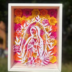 a paper cut image of the virgin mary surrounded by flowers in a white box with pink and orange roses