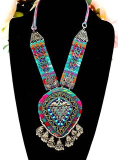 Vibrant, colorful, energetic Afghani Kuchi pendant necklace, that will go with any outfit!   It says "Look at me".  You will be noticed wearing this dramatic necklace! Colorful stiffened fabric pendant and sides, embellished with layers of textures, colors and shapes - eye-catching beads, glowing colored glass, detailed silver tone peacock and flower motif.  A row of delicate jhumka bells are suspended from the bottom. On comfortable velvet backing, to ensure a comfortable fit for you.  Adjustable length via sliding silvertone bead on cotton threads, from 7 in to 12 in.  Pendant 5"H x 3 3/4"W   The jhumka are half jhumka, made so that the jhumka lie flat and don't flip up, complimentary to the design.   Shop more necklaces here: https://www.etsy.com/shop/BoutiqueByMaryam?section_id=2169465 Traditional Adjustable Bib Necklaces For Festivals, Traditional Adjustable Bib Necklace For Festivals, Adjustable Traditional Bib Necklaces For Festivals, Handmade Traditional Bib Necklaces For Festivals, Multicolor Bohemian Necklaces For Festivals, Bohemian Multicolor Necklaces For Festivals, Hippie Multicolor Beaded Necklaces For Festival, Multicolor Hippie Jewelry For Festivals, Hippie Multicolor Jewelry For Festivals