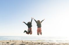 two people jumping in the air on a beach