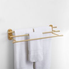 two towels are hanging on a gold towel rack and one is folded in white linens