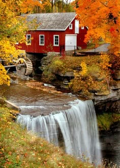 a red house sitting on top of a hill next to a waterfall in the fall