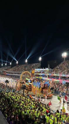 a large group of people standing in front of a circus ring at night time with lights on