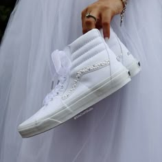 a person in white dress holding up a pair of high top sneakers with pearls on them