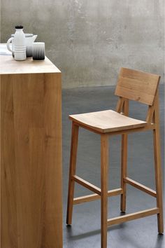 a wooden stool next to a counter with a white vase on it and a teapot in the background