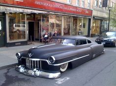 an old car is parked on the side of the road in front of a store