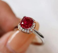 a woman's hand holding an engagement ring with a red stone in the center